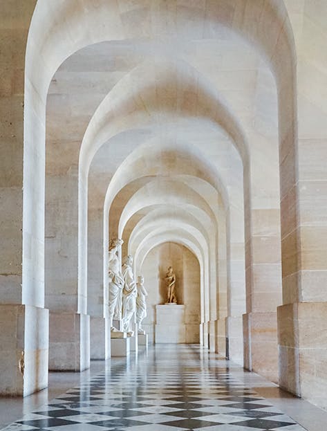 The light-filled Palace Hallway lined with statues on a marble floor in the Château of Versailles, Versailles